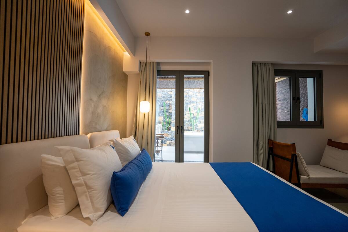 A modern hotel room with a large bed, a seating area, and a view of the outdoors.
