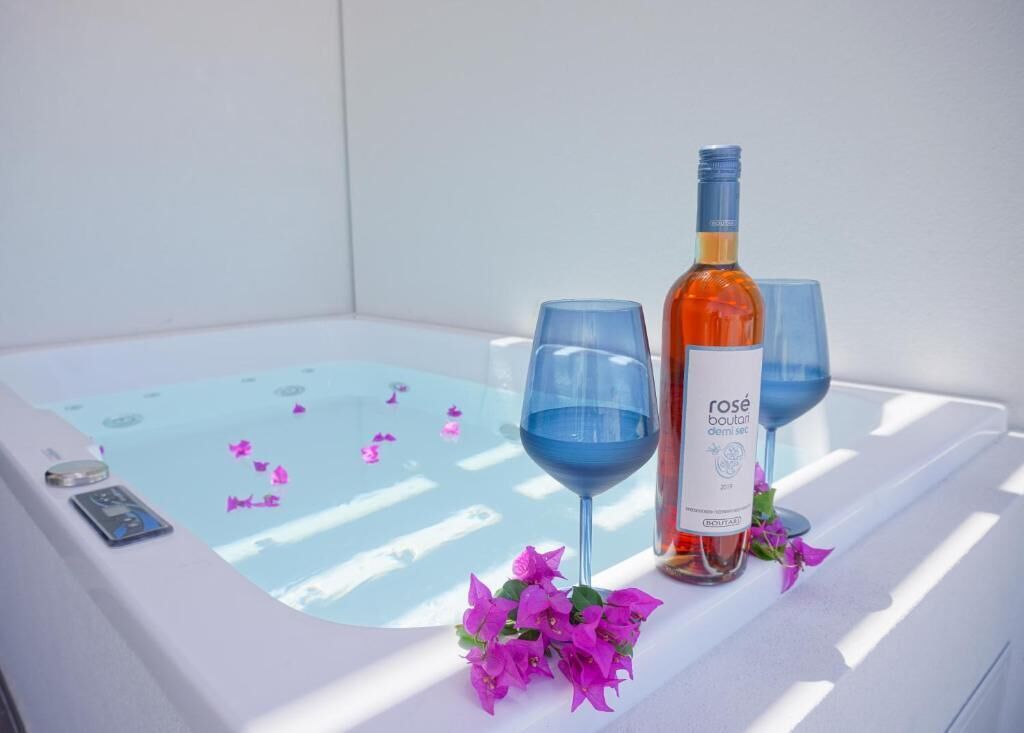 Un bain à remous parsemé de pétales de rose, une bouteille de vin rosé et deux verres.