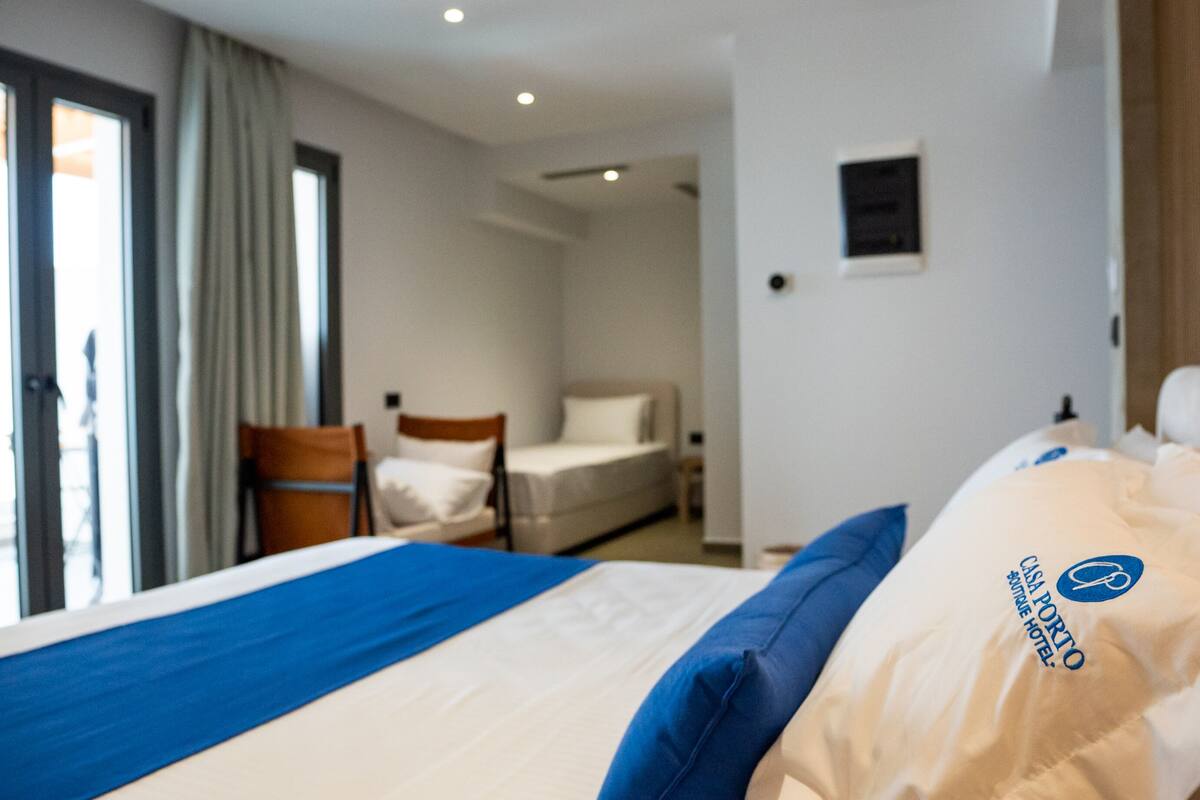 A hotel room with a bed, a chair, a desk, and a window with curtains.