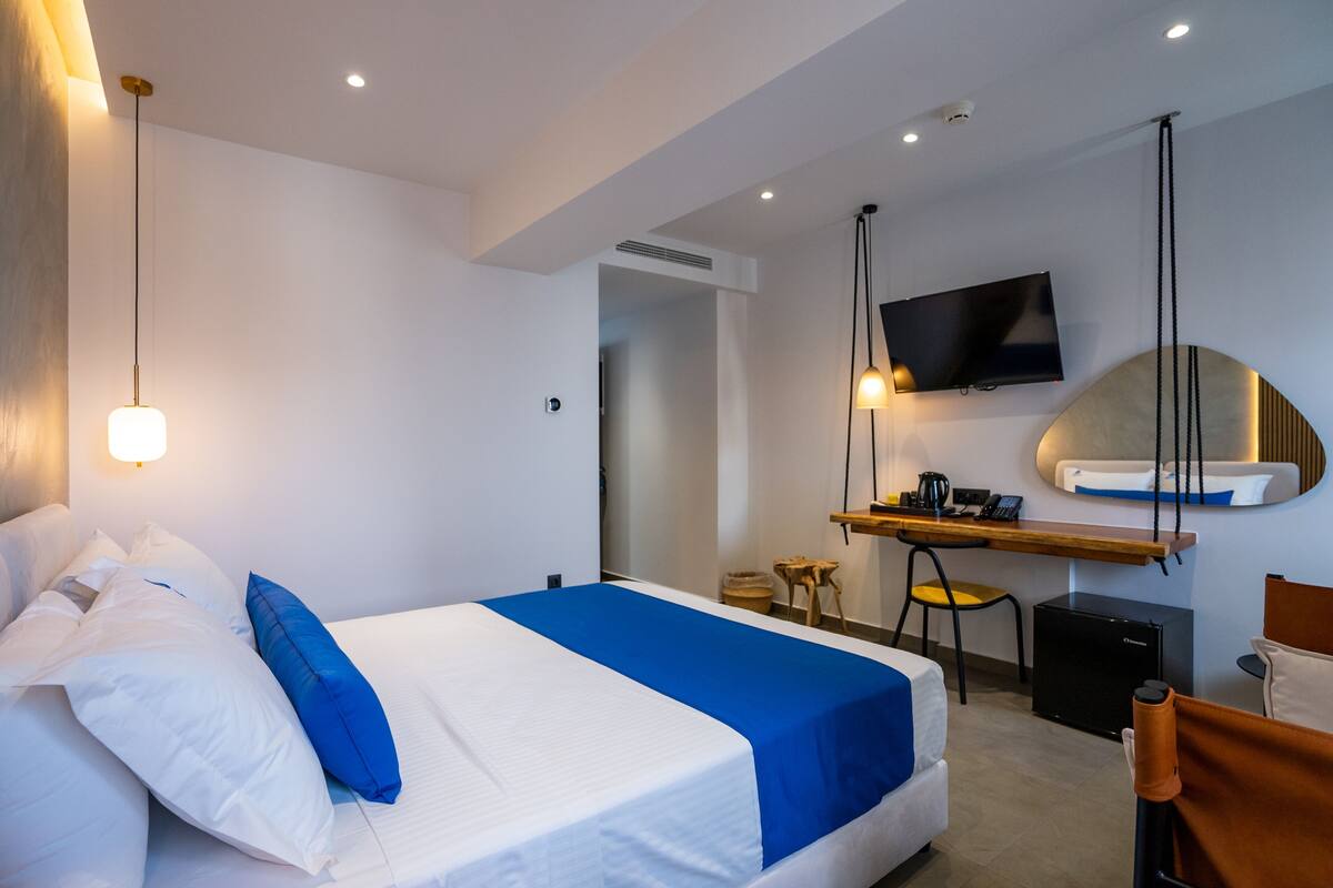 A modern hotel room with a neatly made bed, a desk with a computer, a flat-screen TV, and a small seating area.