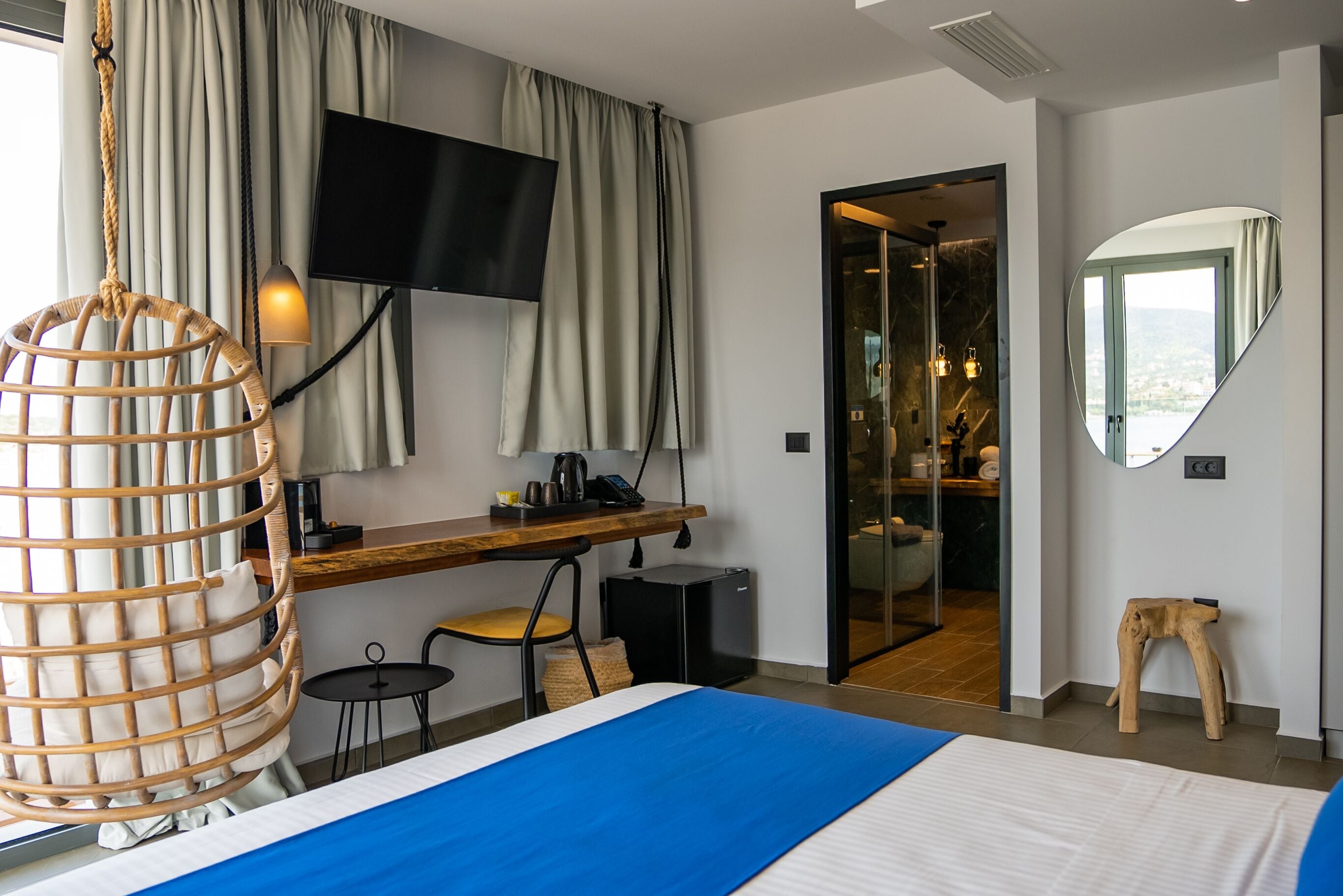 Habitación de hotel con cama, escritorio, televisor, espejo y vistas al exterior.