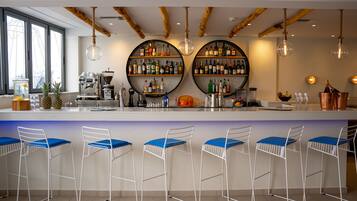 Un bar con una barra blanca, taburetes azules y dos amplias repisas circulares llenas de botellas.
