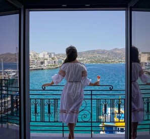 A woman standing on a balcony with a view of the sea and buildings. - Casa Porto Boutique Hotel - Adults only (Agios Nikolaos)