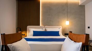 A modern hotel room with a neatly made bed, a bedside table with a lamp, and a wall-mounted light fixture.