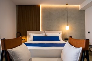 A modern hotel room with a neatly made bed, a bedside table with a lamp, and a wall-mounted light fixture.