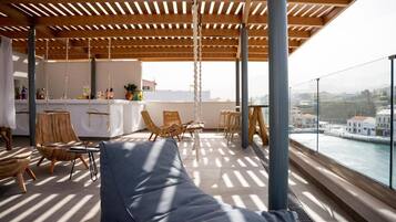 A rooftop terrace with a wooden pergola, seating area, bar, and a view of the city.