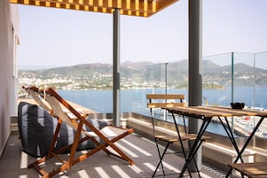 Un balcón con mesa y sillas de madera, un sillón de saco y vistas a un pueblo costero y montañas.