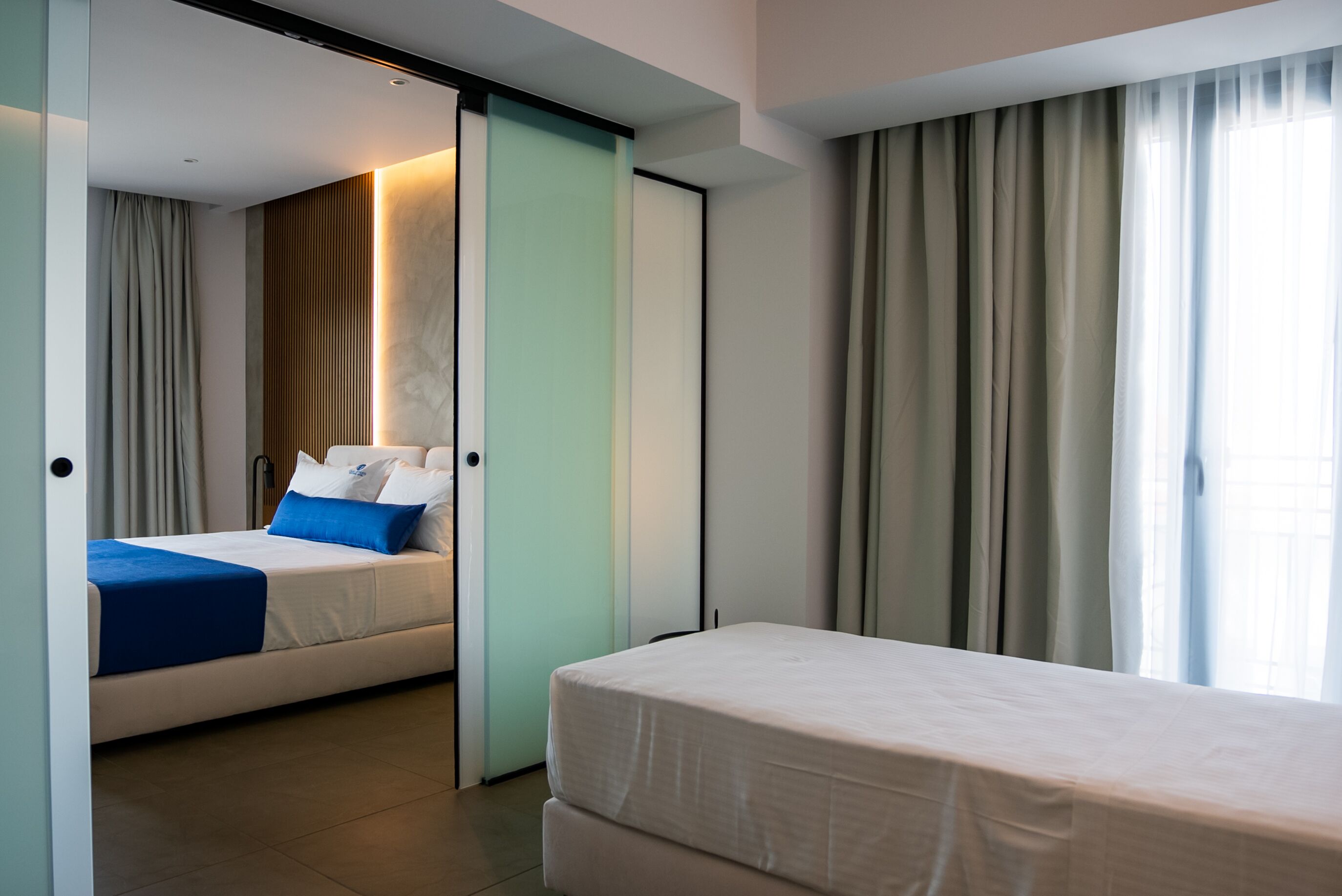 Een moderne hotelkamer met een bed, een afzonderlijk slaapgedeelte en een groot raam met gordijnen.