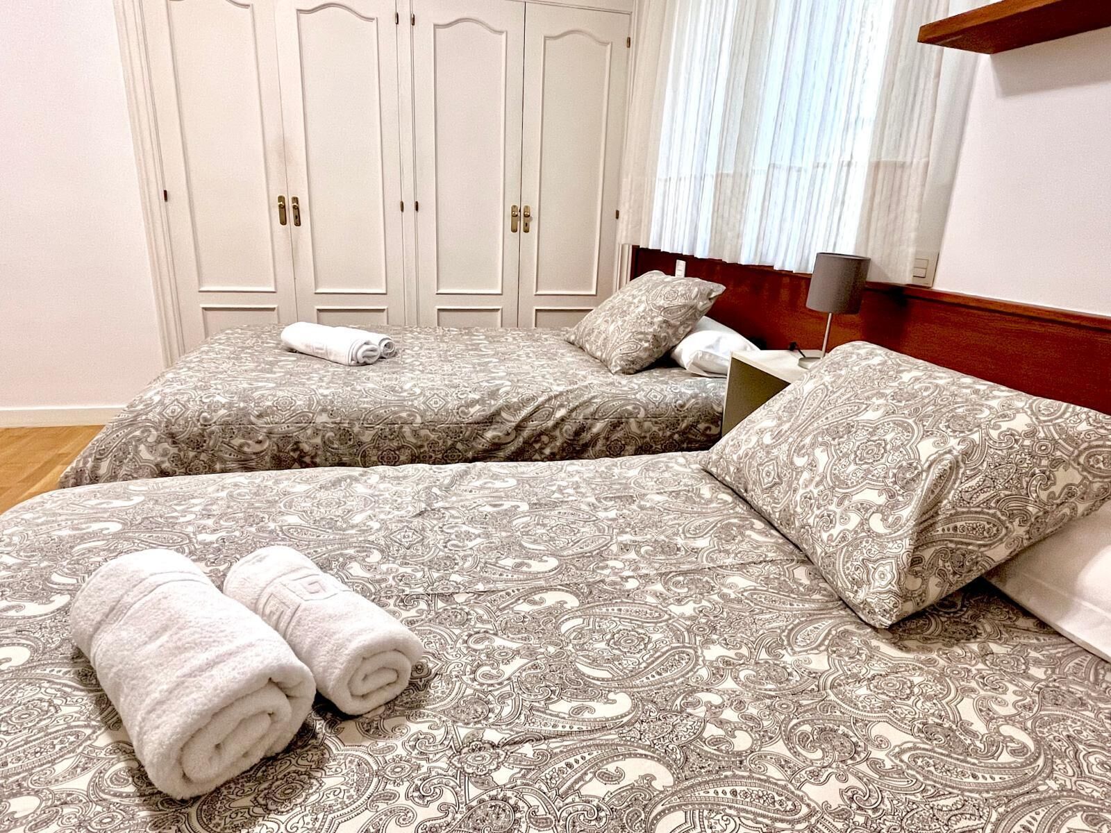Une chambre d’hôtel avec deux lits, chacun agrémenté de draps et d’oreillers à motifs, d’une tête de lit en bois, d’une table de chevet et d’une armoire avec un miroir.