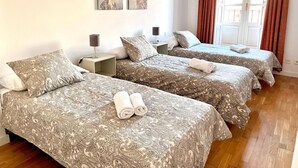 A hotel room with two beds, each with a patterned bedspread, a bedside table with a lamp, and a window with curtains. - Espacios Blanco Plaza Mayor LUX: two rooms, 5 beds, balconies with views of the Plaza Mayor itself! (Valladolid)