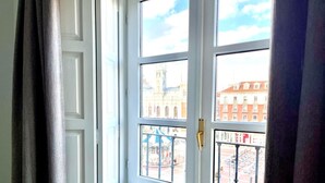 A room with a large window revealing a cityscape with buildings and a clock tower. - Espacios Blanco Plaza Mayor LUX: two rooms, 5 beds, balconies with views of the Plaza Mayor itself! (Valladolid)