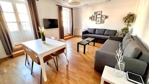 A modern living room with a sofa, a dining table with chairs, a TV, and a wall with framed pictures. - Espacios Blanco Plaza Mayor LUX: two rooms, 5 beds, balconies with views of the Plaza Mayor itself! (Valladolid)