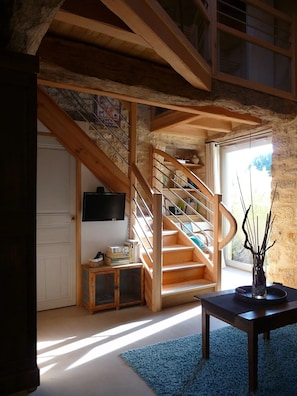 Un vaste espace de vie agrémenté d’un escalier en bois, d’un téléviseur fixé au mur et offrant une vue sur l’extérieur grâce à une grande fenêtre.
