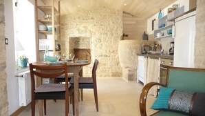 A cozy dining area with a stone wall, wooden furniture, and a kitchen in the background.