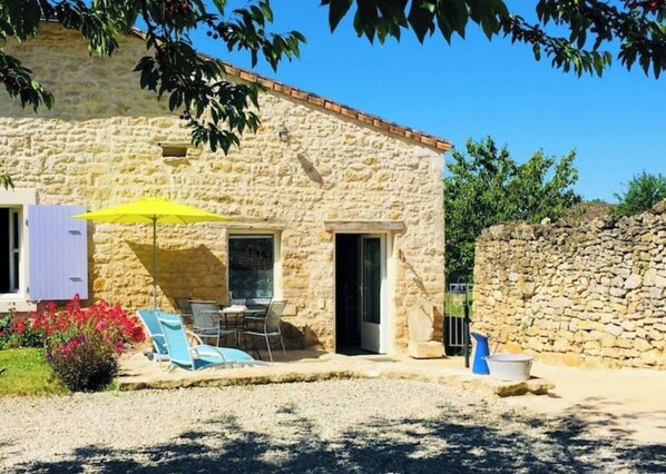 Un bâtiment en pierre doté d’une terrasse, de sièges en plein air et d’un parasol jaune.