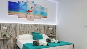 Habitación de hotel con cama, ropa de cama color turquesa y una obra de arte colgada en la pared que representa una playa con un flamenco.