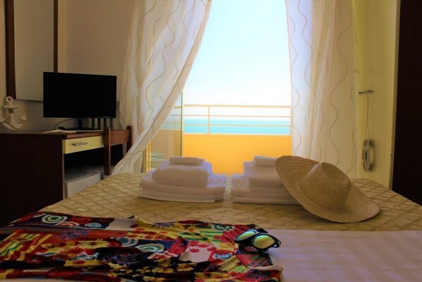 A hotel room with a bed, a desk with a computer, a window with curtains, and a view of the sea. - Hotel Panoramico (Minturno)