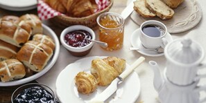 A breakfast setting with croissants, bread, jams, honey, and coffee.