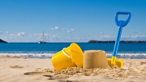 A sandy beach with a blue shovel and yellow buckets.