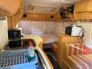 Ein kompaktes Wohnmobil-Interieur mit einer Küchenzeile, einem Bett und einer kleinen Sitzecke.