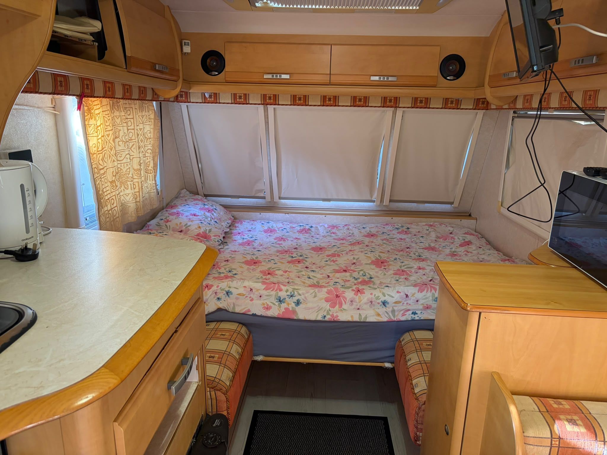 Interni di un camper compatto con letto, angolo cottura e televisore.