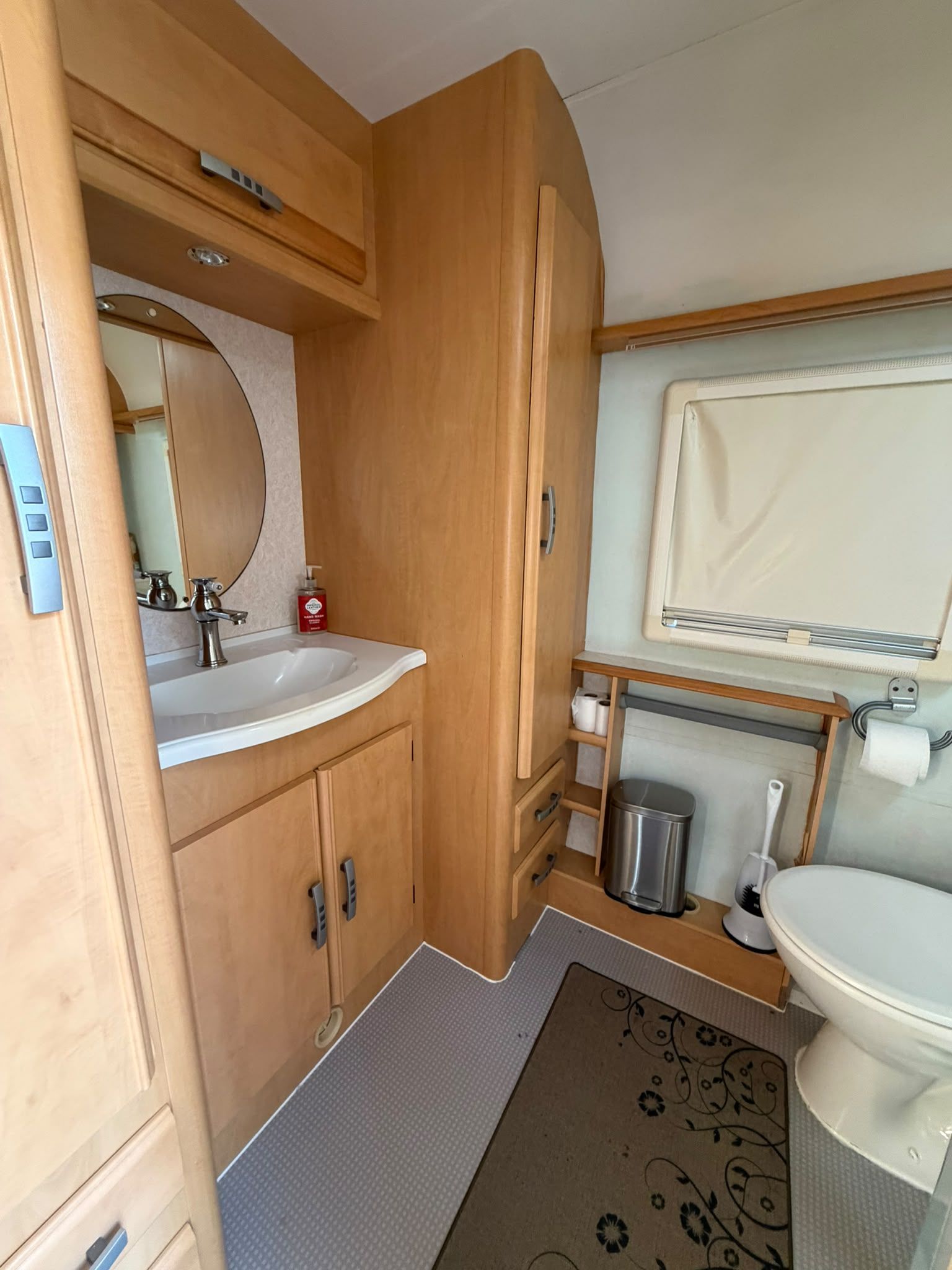 A compact RV bathroom with a sink, toilet, and storage cabinets.