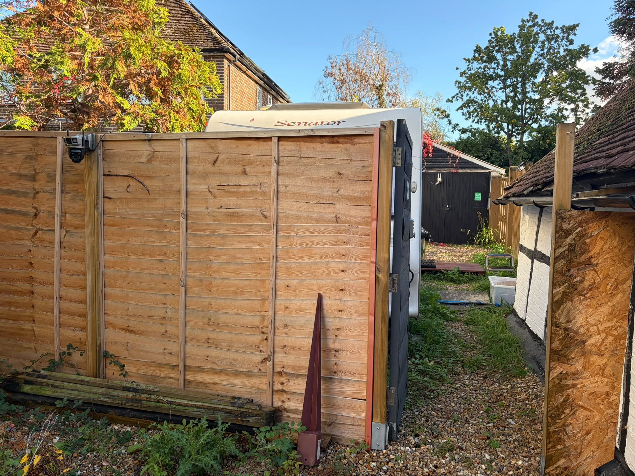 A wooden shed with a 'Senator' sign, a black door, and a small garden area with gravel and plants.