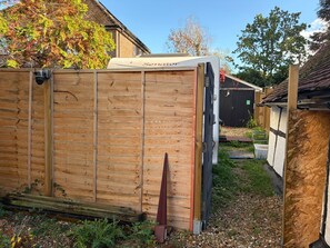 Ein hölzernes Gartenhaus mit einem 'Senator'-Schild, einer schwarzen Tür und einem kleinen Gartenbereich mit Kies und Pflanzen.