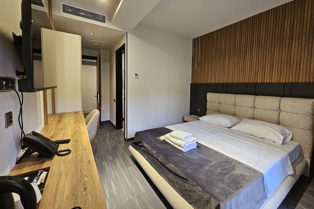 Quarto de hotel com uma cama, uma escrivaninha com telefone e uma televisão na parede.