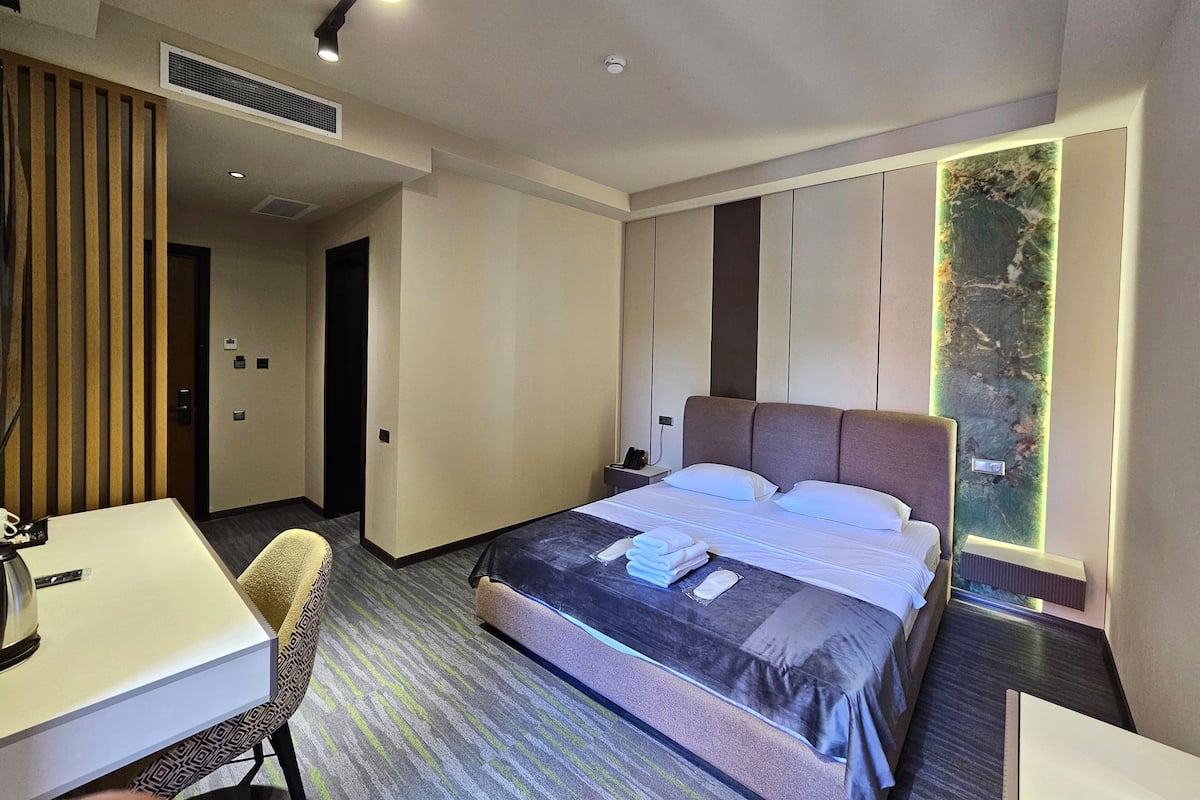 Quarto de hotel moderno com uma cama grande, uma escrivaninha e uma cadeira. Há uma janela com vista para áreas verdes.