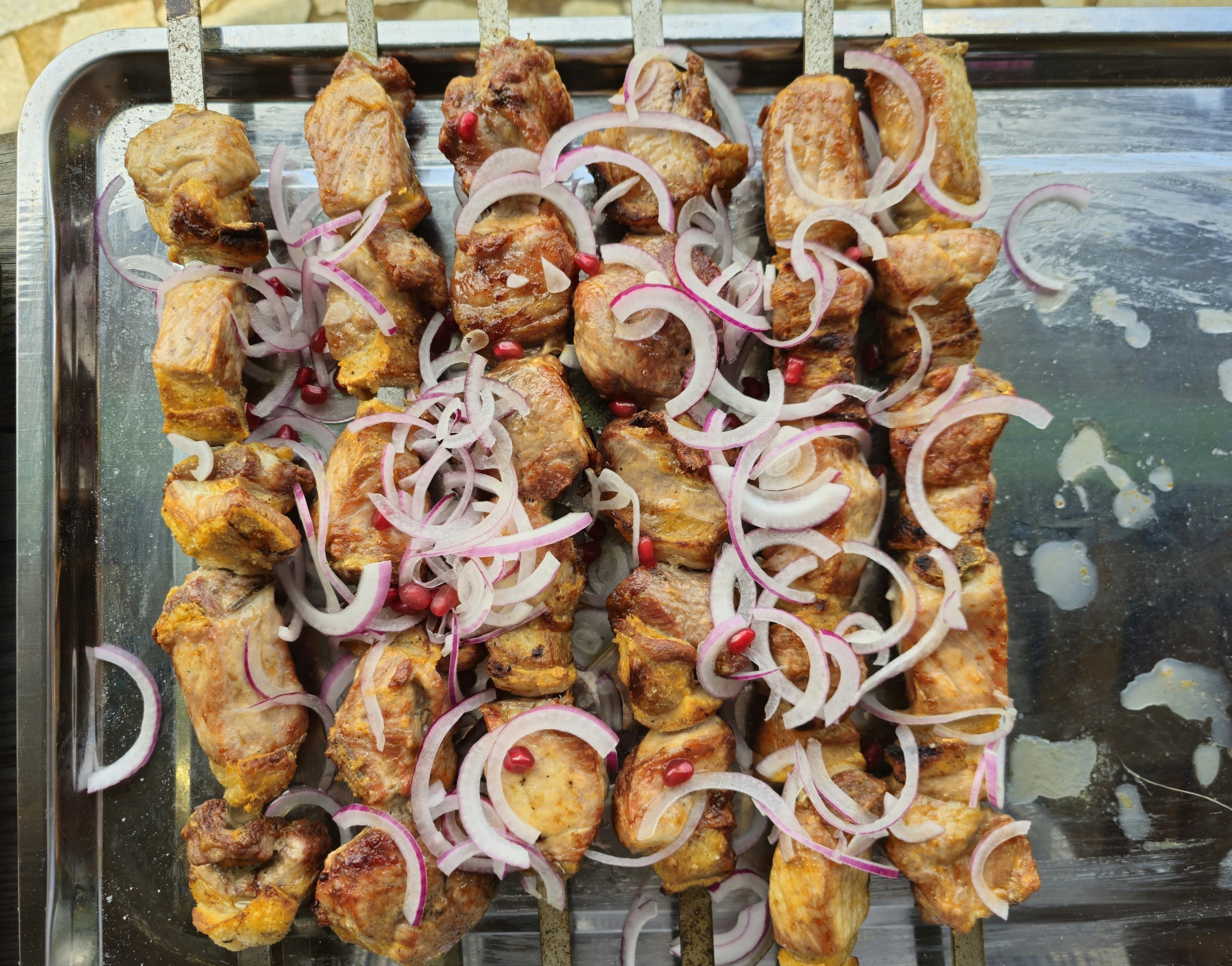 Una bandeja con brochetas de carne a la parrilla, cebollas rojas y semillas de granada.