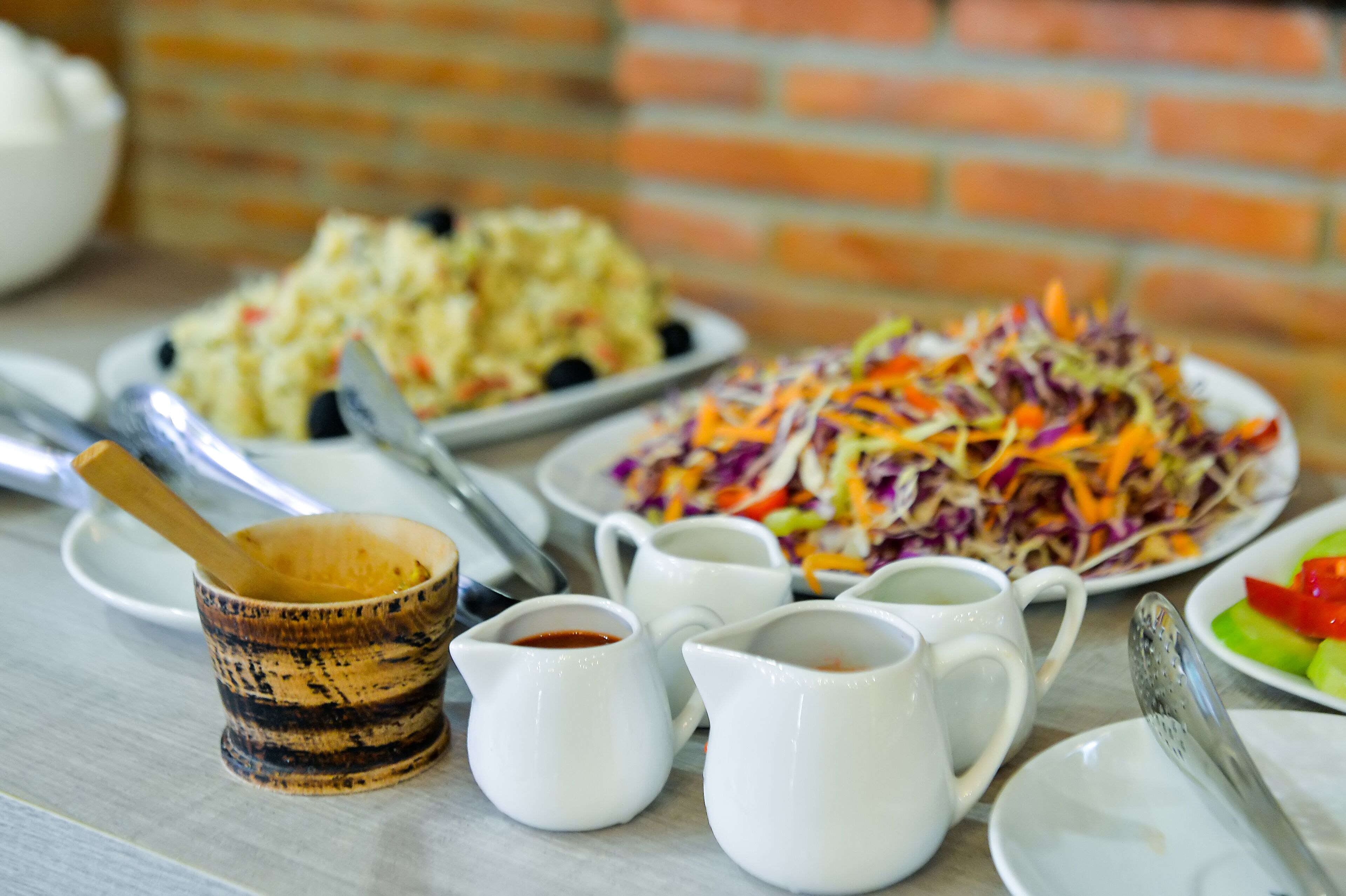 A table with various dishes and condiments, including a coleslaw salad, potato salad, and a small wooden bowl with a spoon.