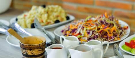 Una mesa con diversos platos y condimentos, incluyendo una ensalada de col, ensalada de papas y un tazón pequeño de madera con una cuchara.