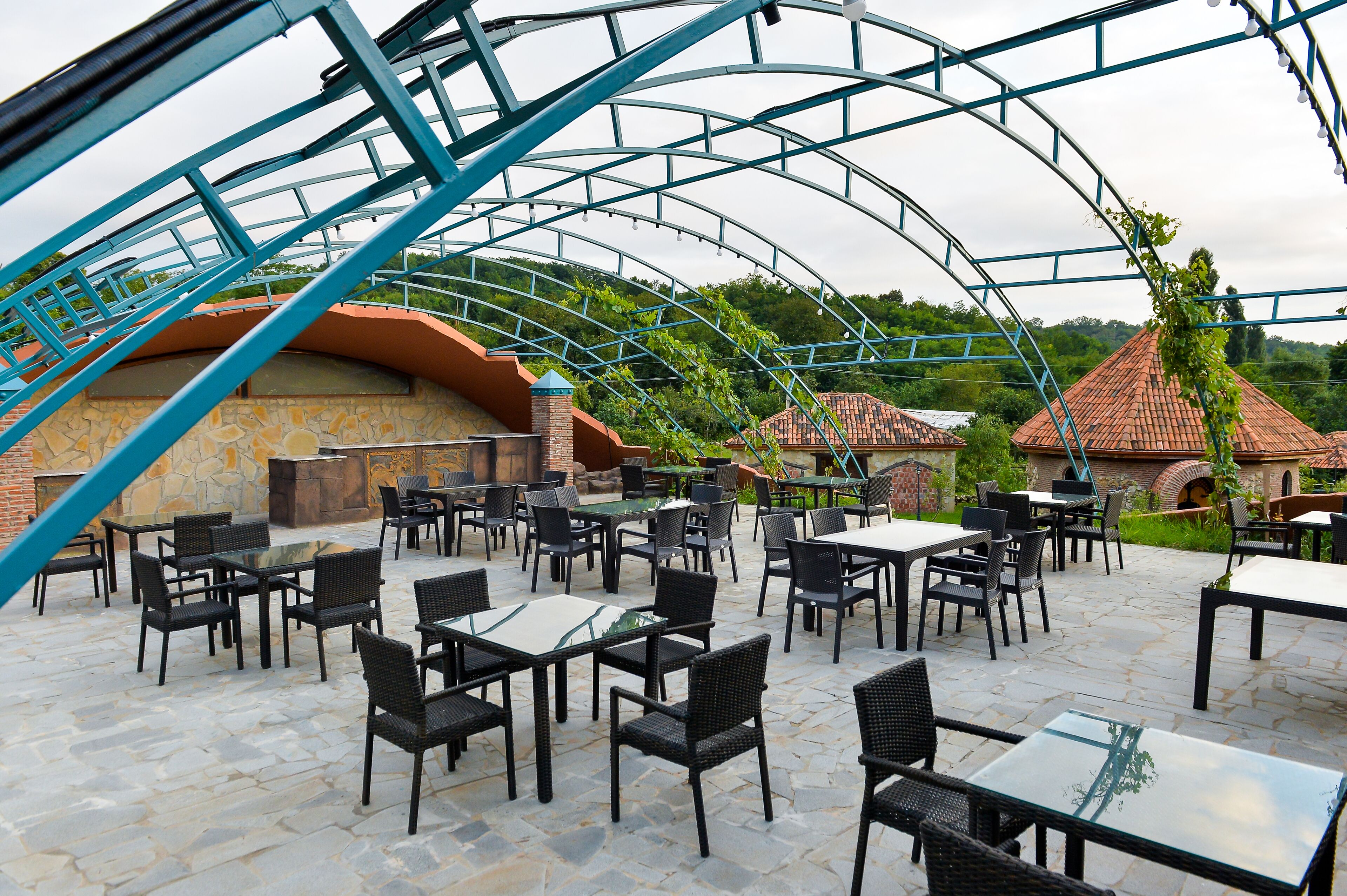 An outdoor patio with stone flooring, black wicker chairs, and tables.