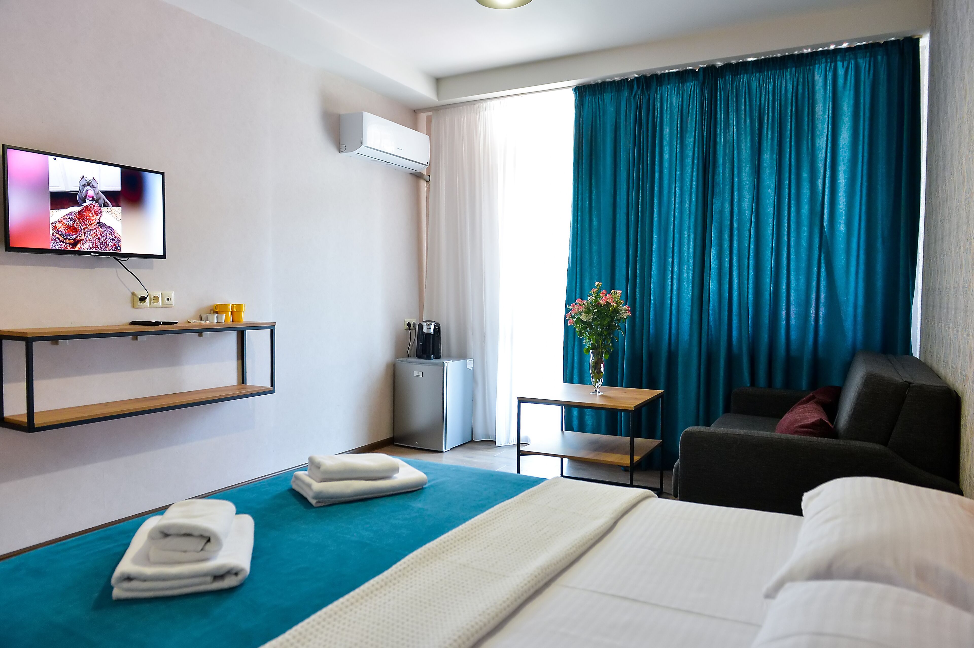 A hotel room with a bed, a desk, a chair, a TV, a coffee machine, and a window with curtains.