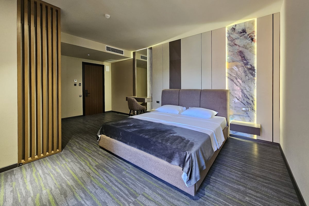 Quarto de hotel moderno com uma cama grande, um espaço de estar e uma parede decorativa em mármore.