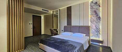 A modern hotel room with a large bed, a seating area, and a marble accent wall.
