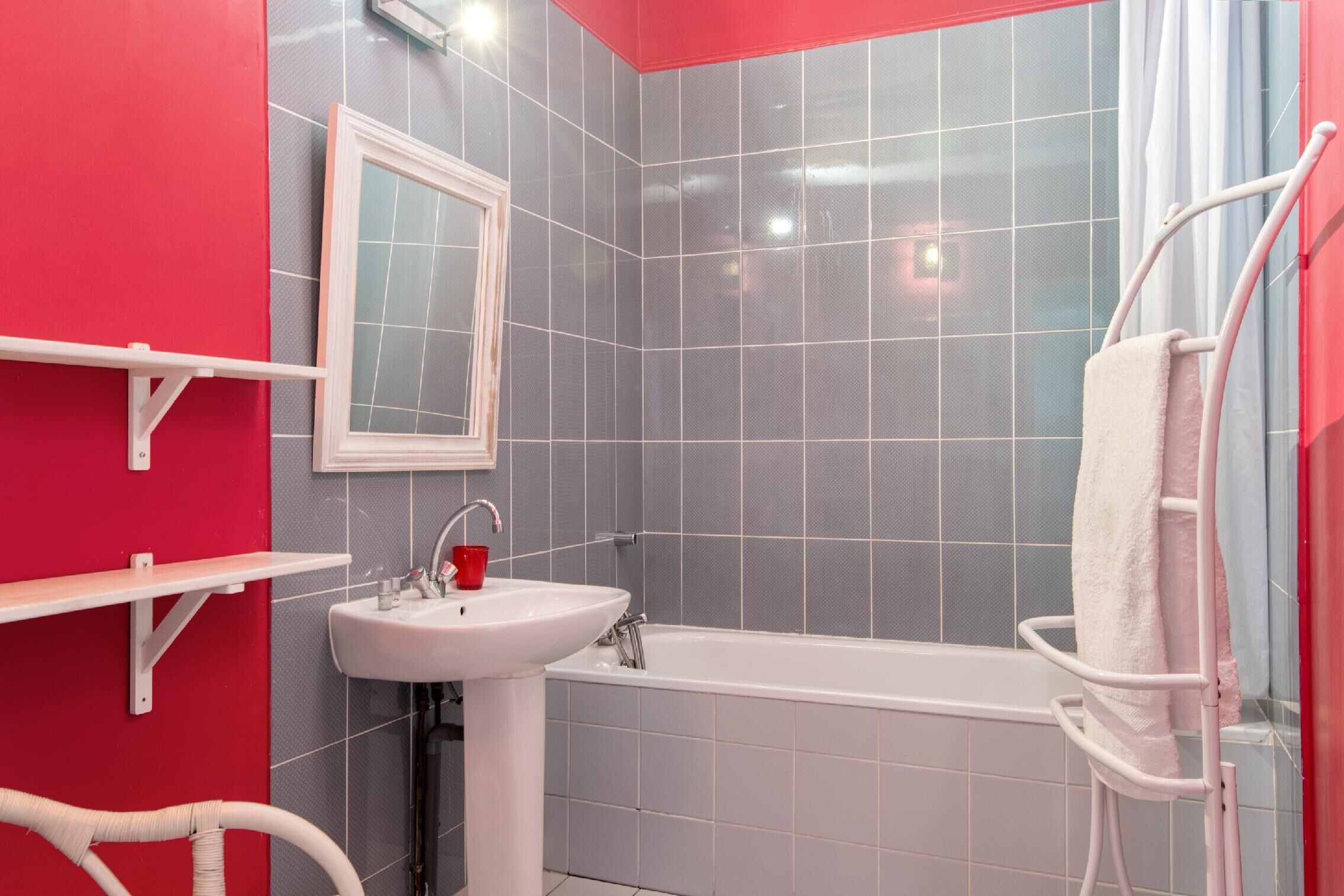 Une salle de bain avec un lavabo blanc, une étagère rouge, une baignoire blanche et un porte-serviettes blanc.