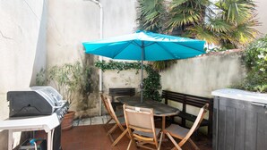 Un patio con una parrilla, una mesa y sillas de madera, un paraguas azul y un banco de madera.