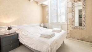 Un dormitorio con cama, mesita de noche, lámpara y un espejo grande y decorativo.