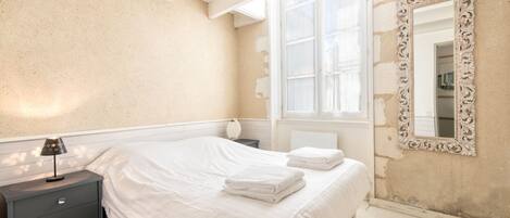 A bedroom with a bed, bedside table, lamp, and a large ornate mirror.