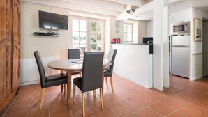 Un comedor con una mesa redonda y cuatro sillas, un televisor montado en la pared, y una zona de cocina con microondas y refrigerador.