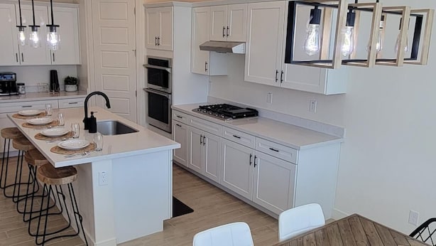 A modern kitchen with white cabinets, a central island, and a dining area with a wooden table and chairs.