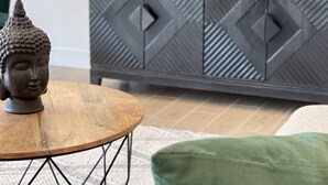 A modern living room with a wooden coffee table, a Buddha statue, a grey patterned cabinet, and a green cushion.