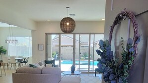 A spacious living room with a large sofa, a dining area with chairs and a table, and a view of a swimming pool through large glass doors.