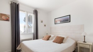 Une chambre à coucher avec un grand lit, une table de chevet, une lampe, une fenêtre avec des rideaux et un tableau encadré au mur.