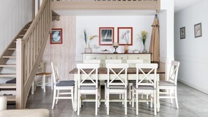 Un coin repas avec un escalier en bois, des chaises blanches, une table en bois et des œuvres d’art encadrées accrochées au mur.