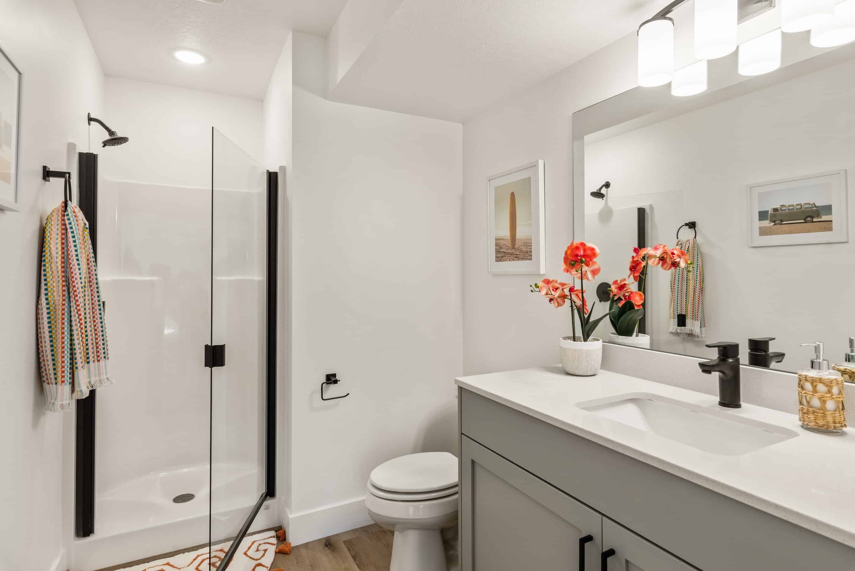 Un bany modern amb un espai de dutxa de vidre, un vàter blanc i un lavabo amb rentapel i mirall.