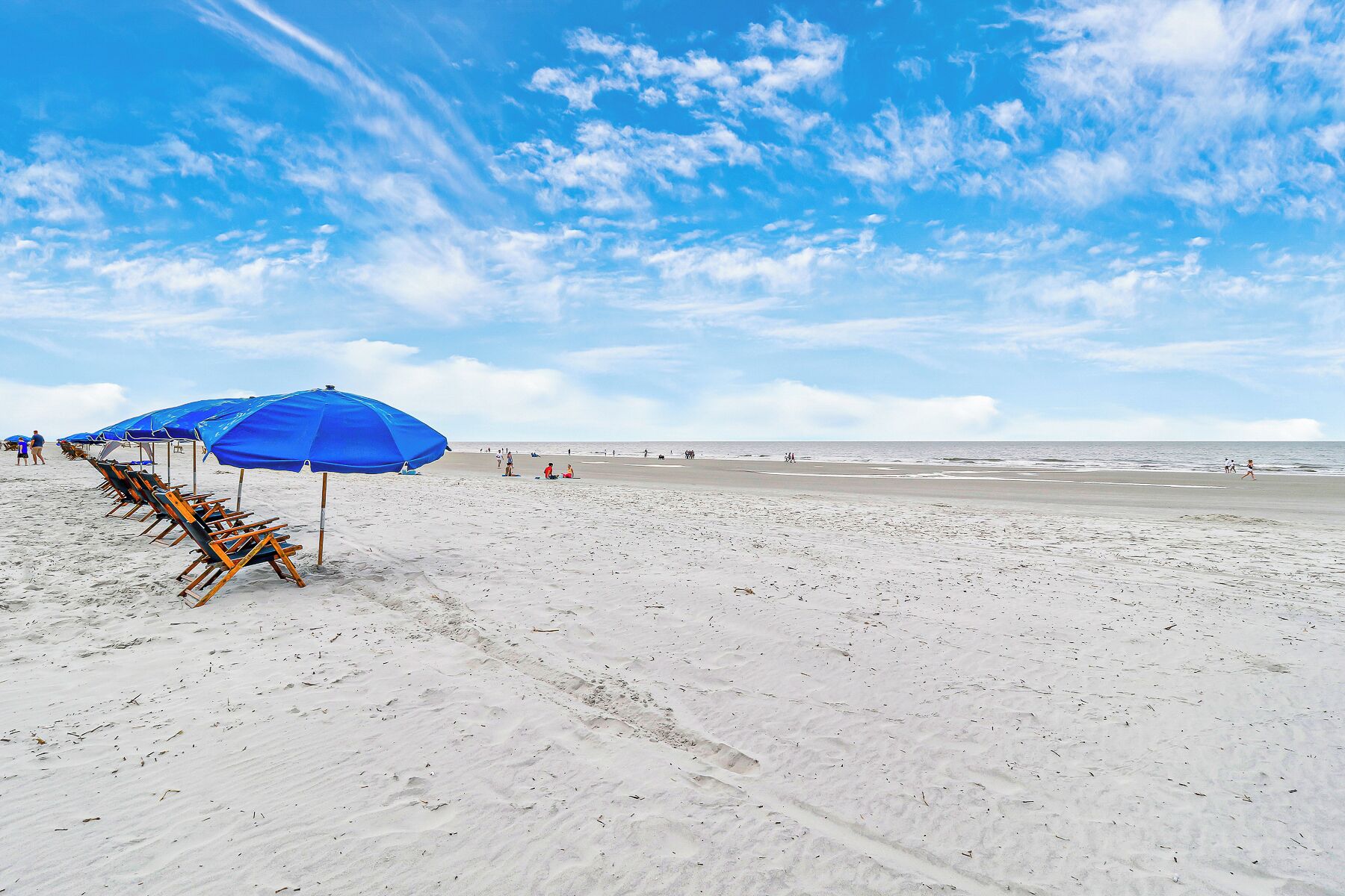 A beach with rows of blue umbrellas and beach chairs, a sandy shore, and the ocean in the background.