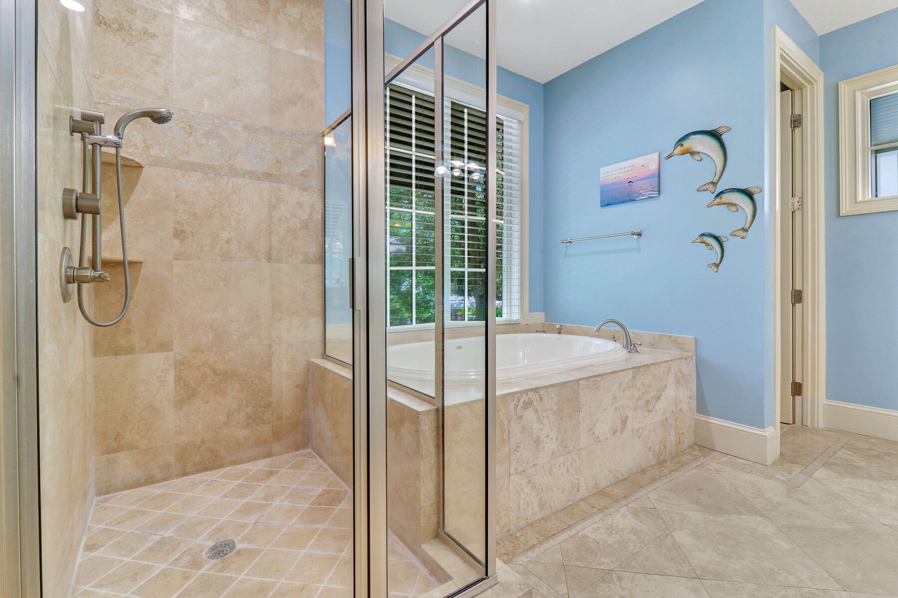 Une salle de bain avec une douche à parois de verre, une baignoire et une fenêtre équipée de stores.